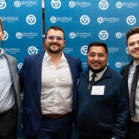 Alex Hogarth poses with 3 men in front of GVSU background